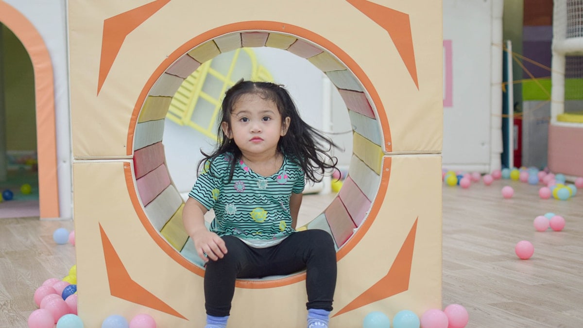 a little girl sitting on a cube in a play room